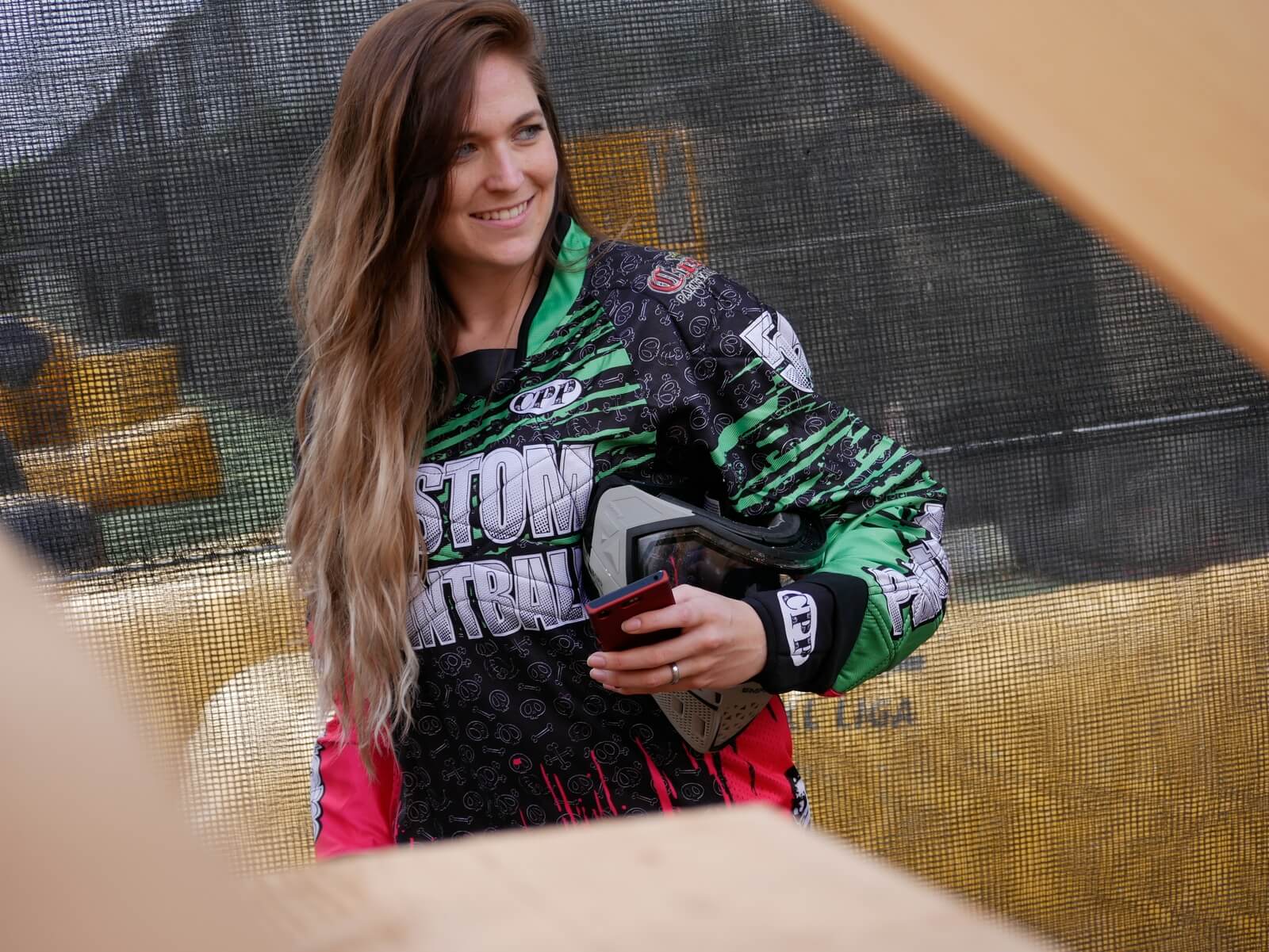 Paintballspielerin am Spielfeldrand mit Paintballmaske in der Hand